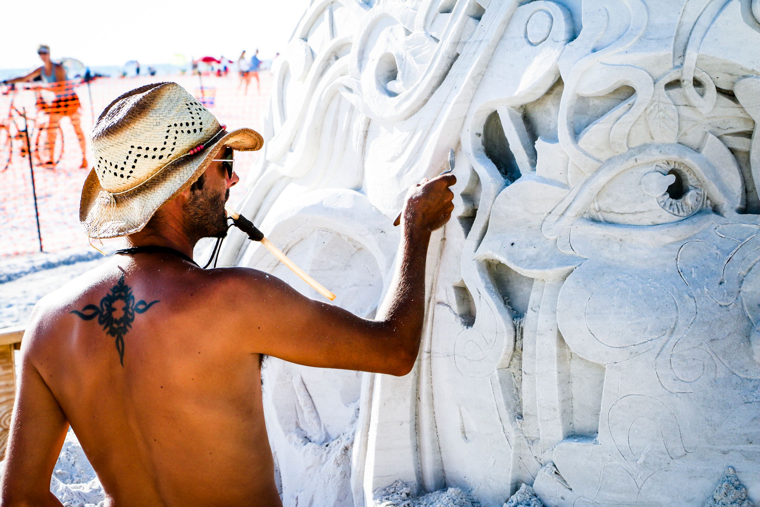 Person carving sand sculpture with a spoon at Siesta Key Crystal Classic, a sand-sculpting festival.