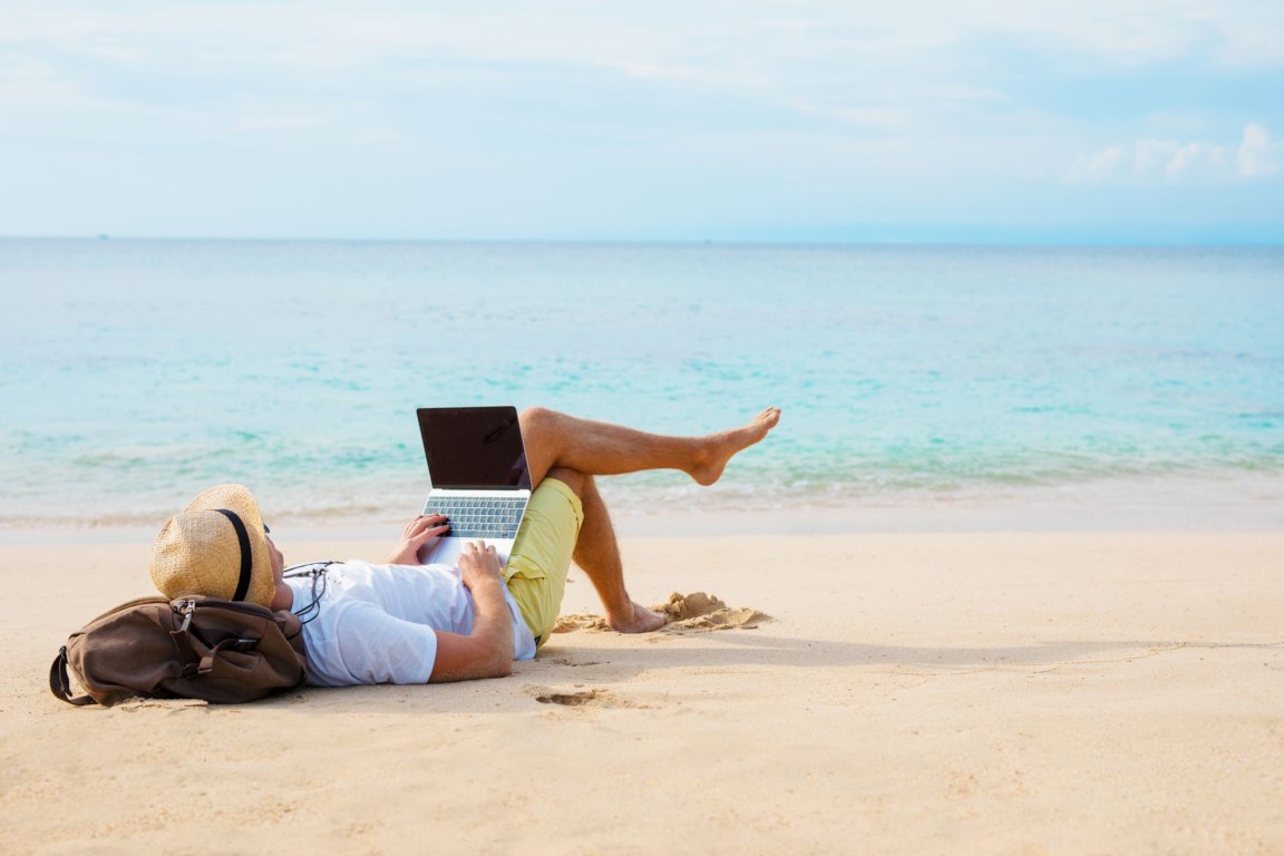 Man working laptop while relaxing on the beach.