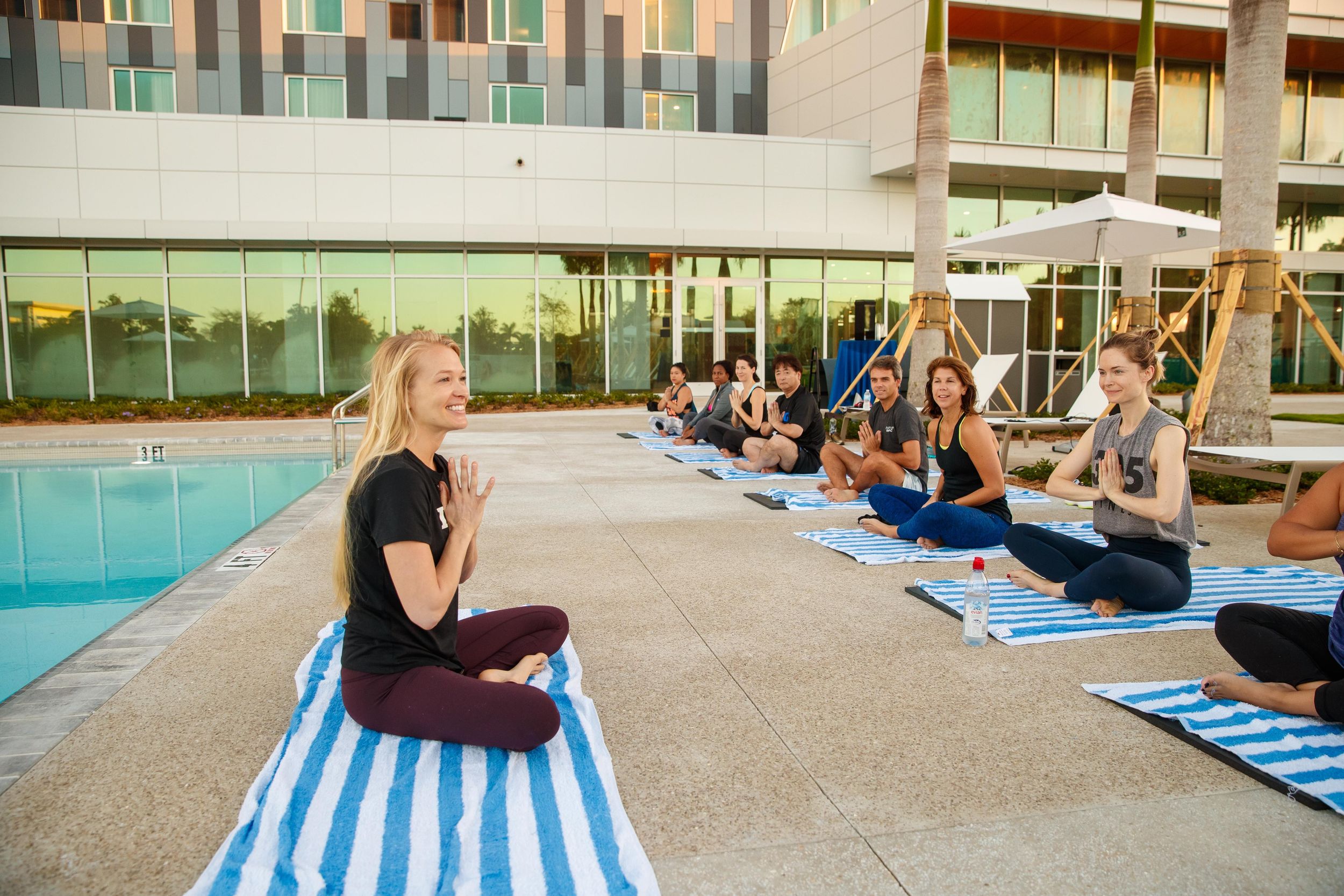 A group of people take a yoga class by a hotel pool outside.