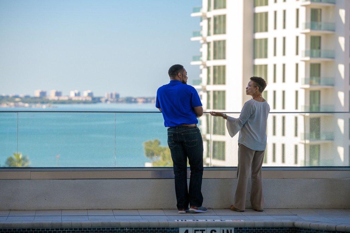 Two people have a conversation on a high-rise's balcony.