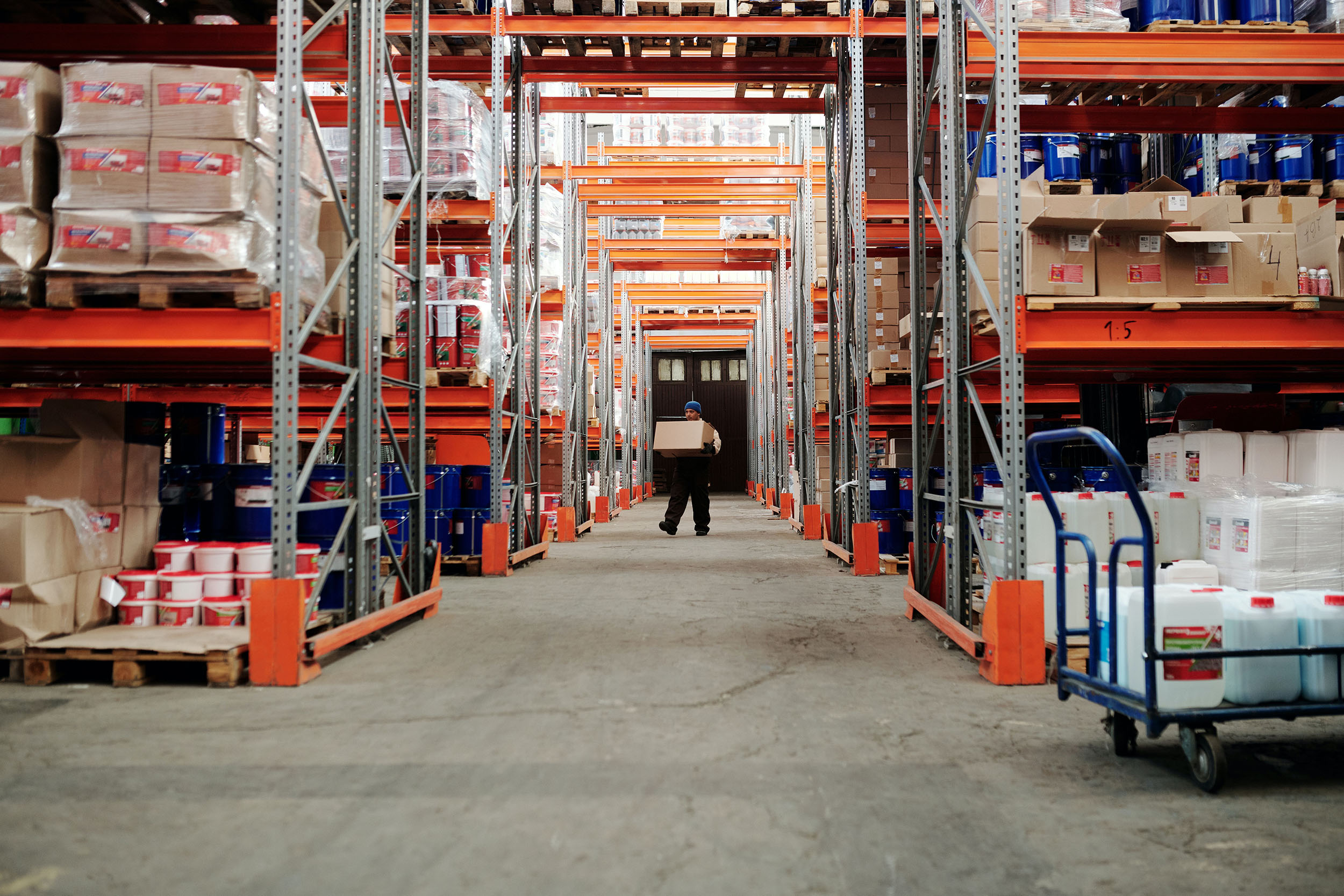 Man standing in aisle of warehouse carrying a box.
